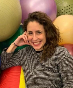 Hispanic woman, dark brunette hair, black and white stripped shirt in from of colored bouncing balls