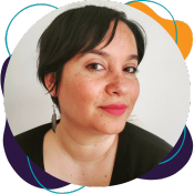 An Iranian femme with olive skin tone wears bright pink lipstick. She smiles at the camera. She has short, whispy hair, a long silver feather earring, and she is wearing a black shirt.